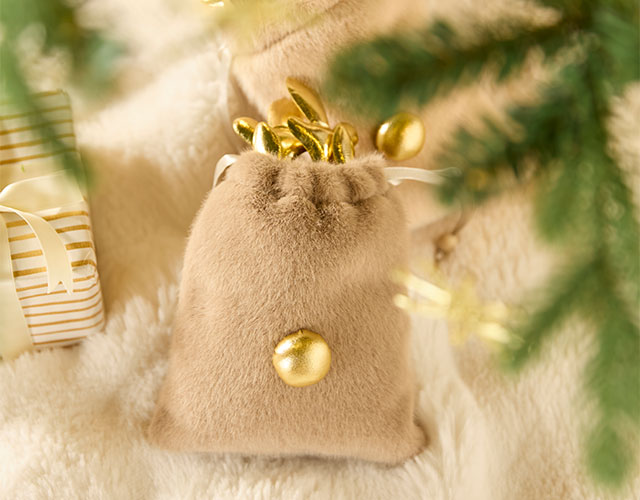 Weihnachtsdeko: beigefarbenes Samtsäckchen mit goldenen Christbaumkugeln auf weichem Fell
