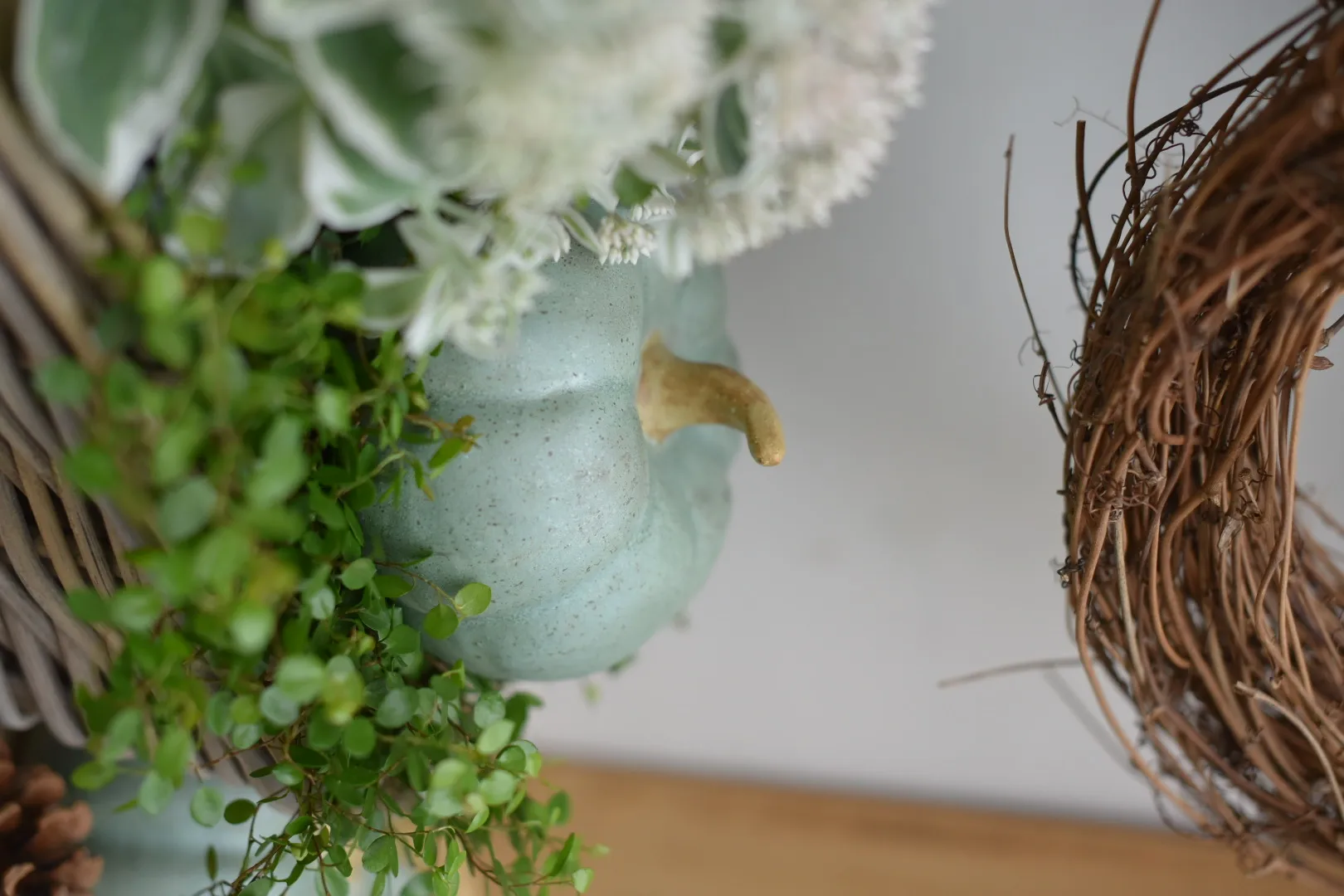 Herbstdeko: grüner Keramikkürbis mit Naturkranz und weißen Blüten als Tischdekoration