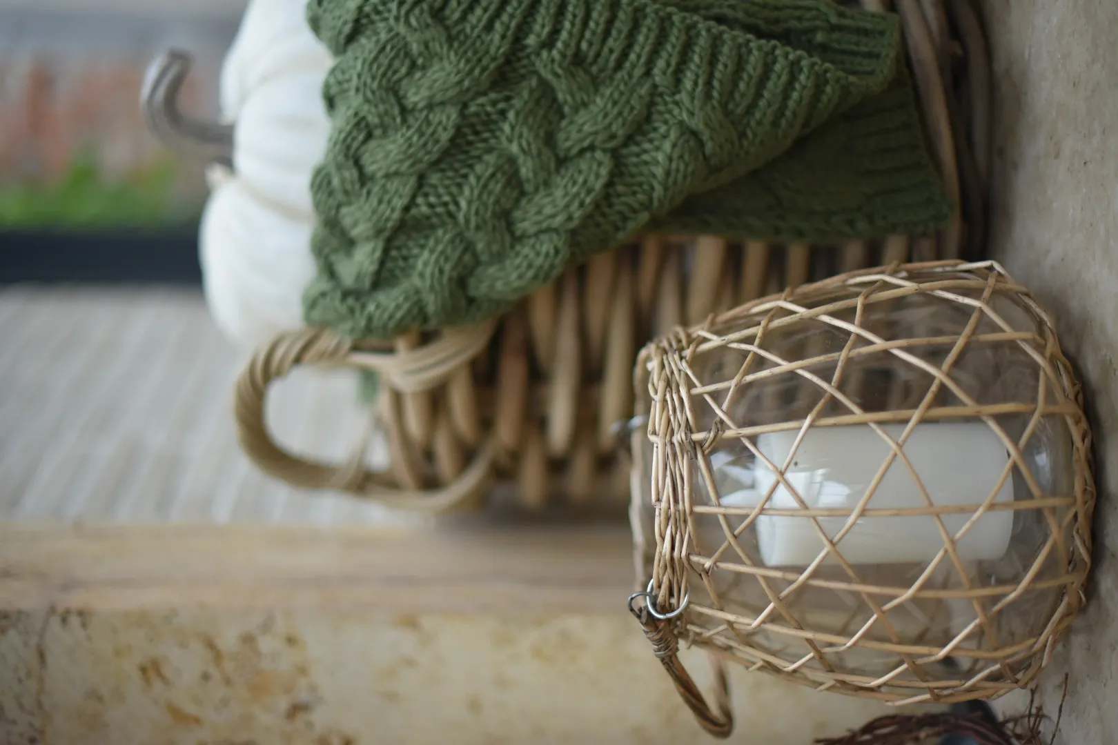 Herbstdeko: Rattanwindlicht mit Kerze, grüner Strickdecke und weißem Zierkürbis