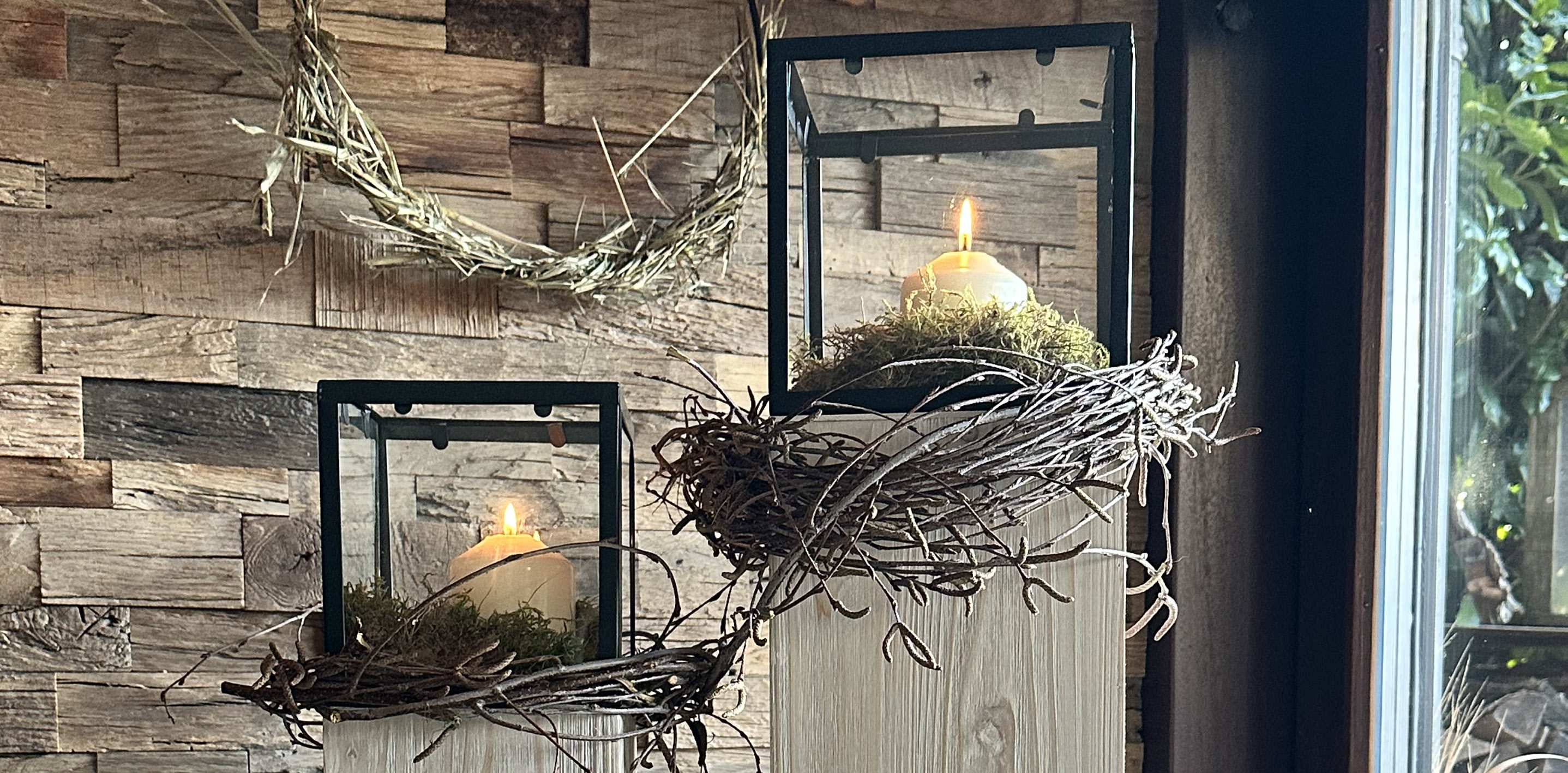 rühlingsdeko: schwarze Laternen mit weißen Kerzen in Moosnestern auf hellen Holzsäulen