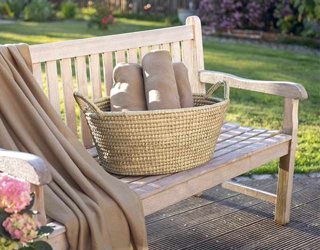 Korbwaren: geflochtener Korb mit Decken auf Holzbank als dekorative Garten- oder Terrassendeko