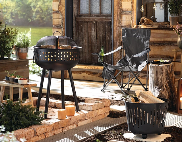Gartendeko: dekorierter Grillplatz mit Kugelgrill, Gartenstuhl und Holz als Sommer‑Outdoor‑Szene