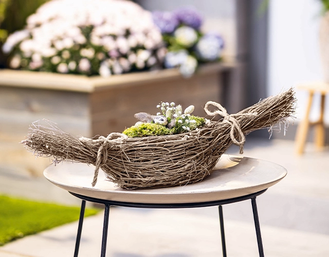 Naturdeko: längliche Korbschale aus Zweigen mit Moos und weißen Frühlingsblumen als Tischdeko