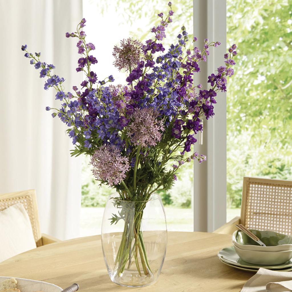Violetter und rosa Blumenstrauß in einer Glasvase auf einem Holztisch
