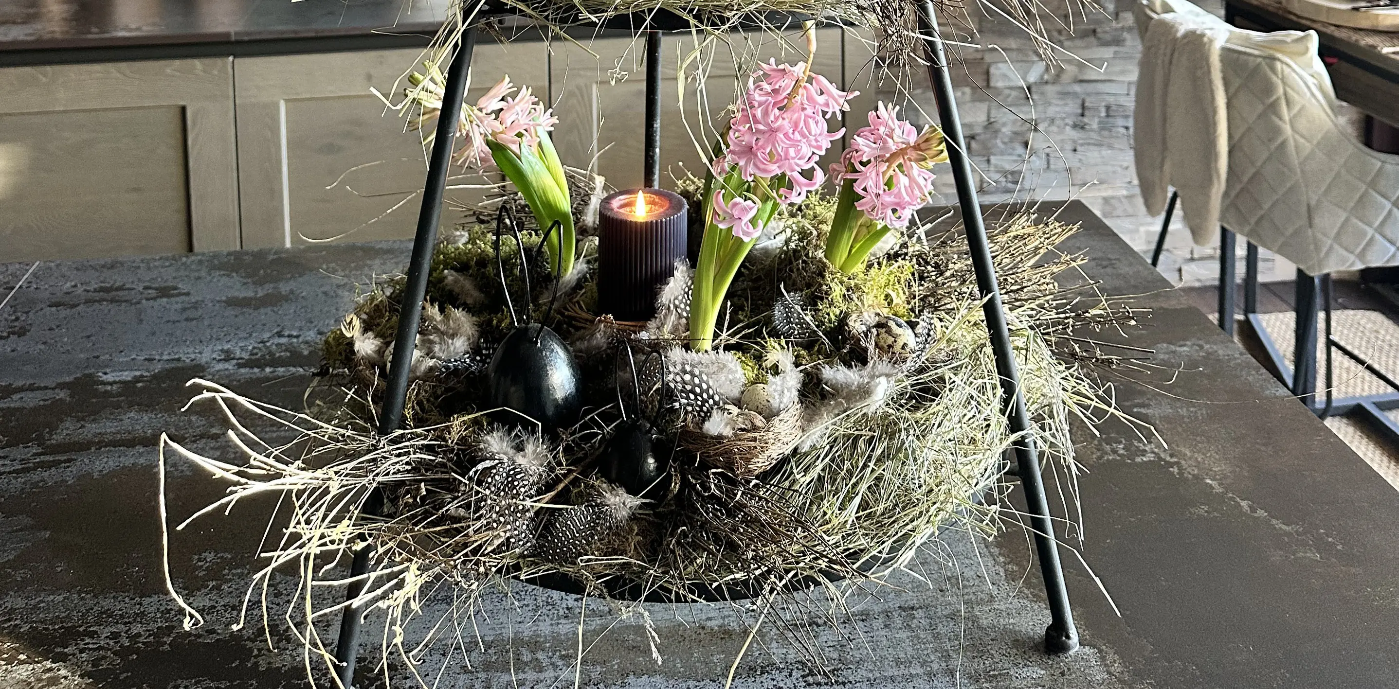Osterdeko: Moosnest mit rosa Hyazinthen und schwarzen Deko‑Eiern in Metallständer