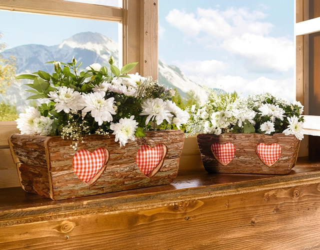 Pflanzkasten: rustikale Holzkästen mit weißen Blumen und Herzdekoration als Alpen‑Fensterdeko