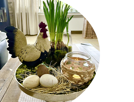 Osterdekoration auf Tablett mit Hahnfigur, Glaswindlicht, Eiern und Frühlingspflanzen im Wohnraum