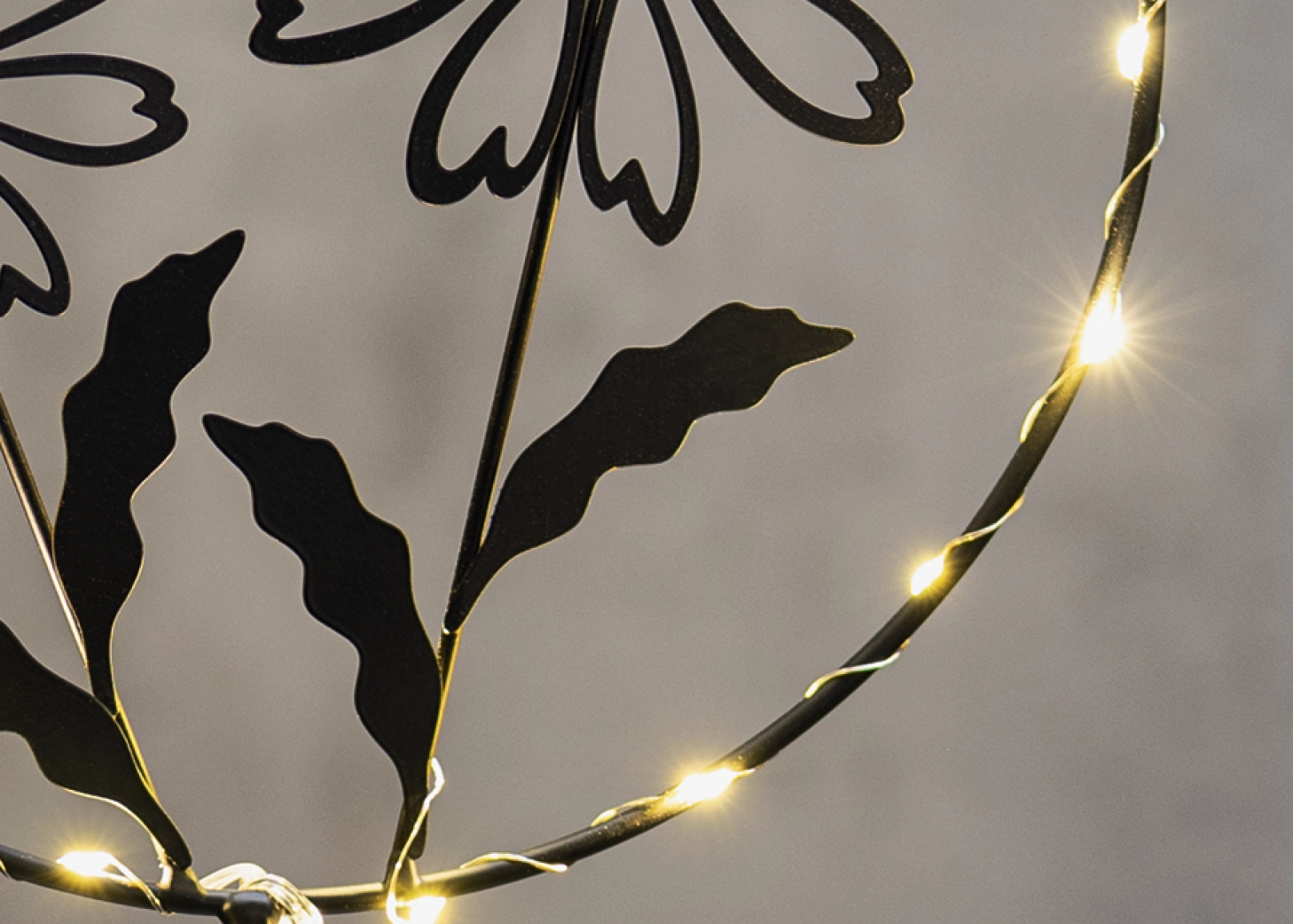 LED-Leuchtdeko: schwarzer Metallring mit Blumenmotiv und warmweißer Lichterkette als Fensterdeko