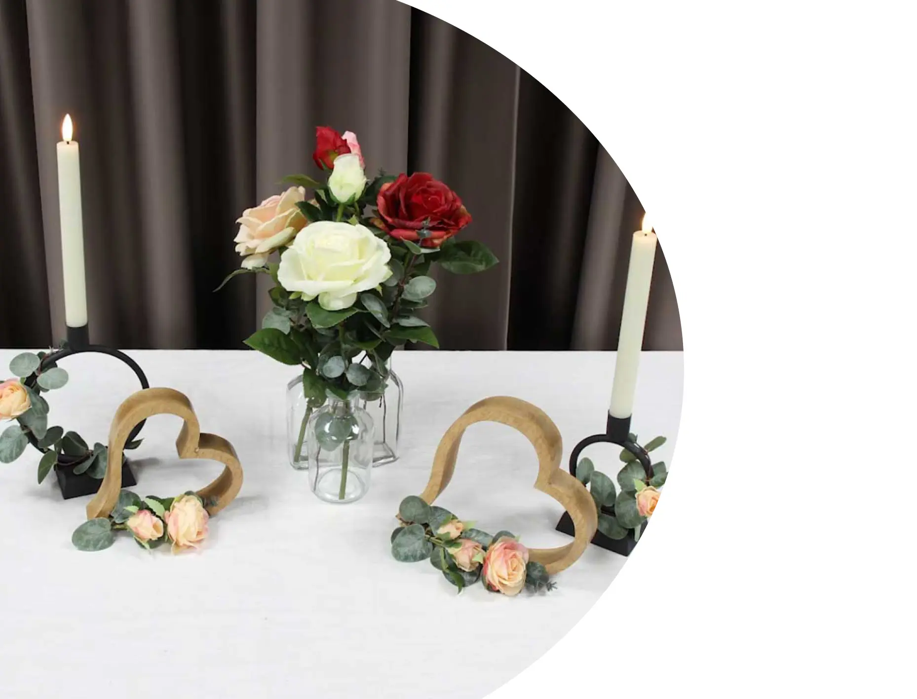 Tischdeko: Glasvase mit bunten Rosen, Holzherzen und Kerzen als romantische Dekoration