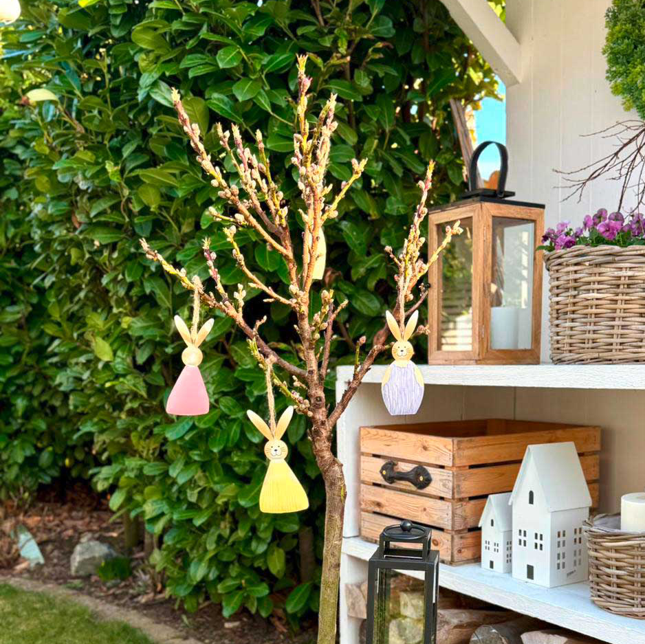 Osterdeko: bunte Hasenanhänger am Zweig mit Pflanzkorb und Gänseblümchen