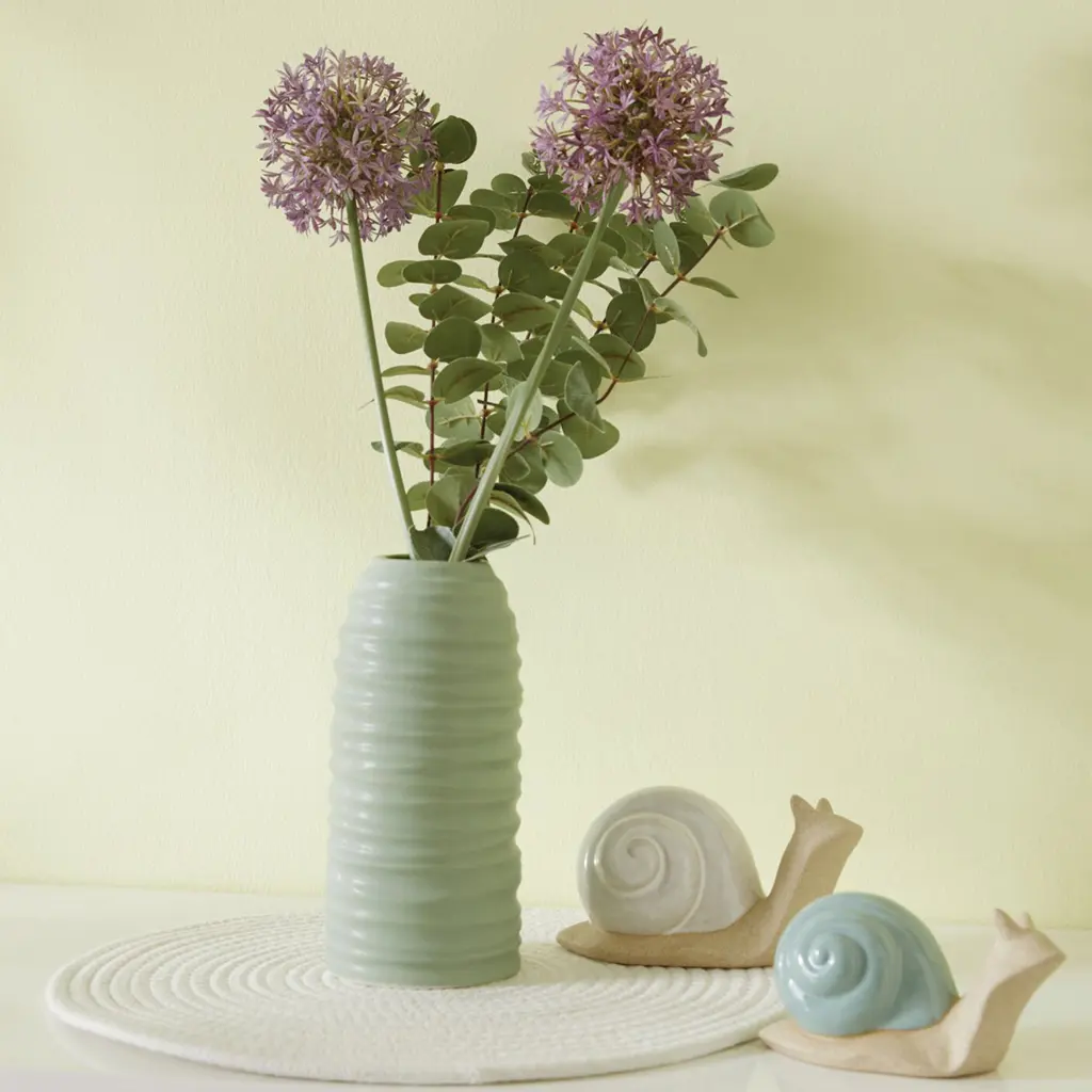 Zwei Alliumblüten in hoher grüner Vase mit Deko-Schnecken