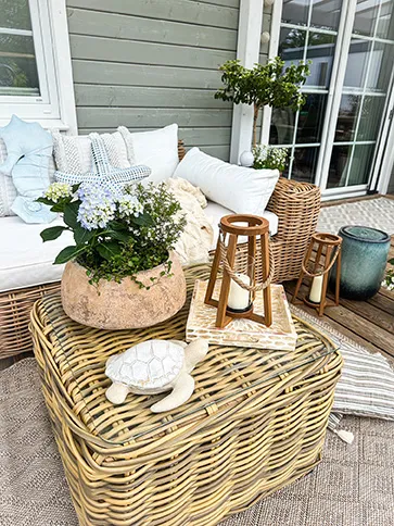 Gartendeko: Rattanmöbel mit Kissen, Laternen, Pflanzschale und blauem Blütenschmuck auf Terrasse