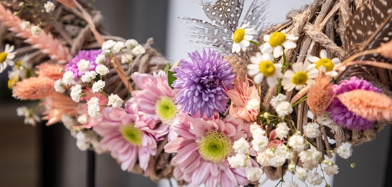 Frühlingsdeko: naturfarbener Kranz mit rosa, lila und weißen Kunstblumen als bunte Osterdekoration