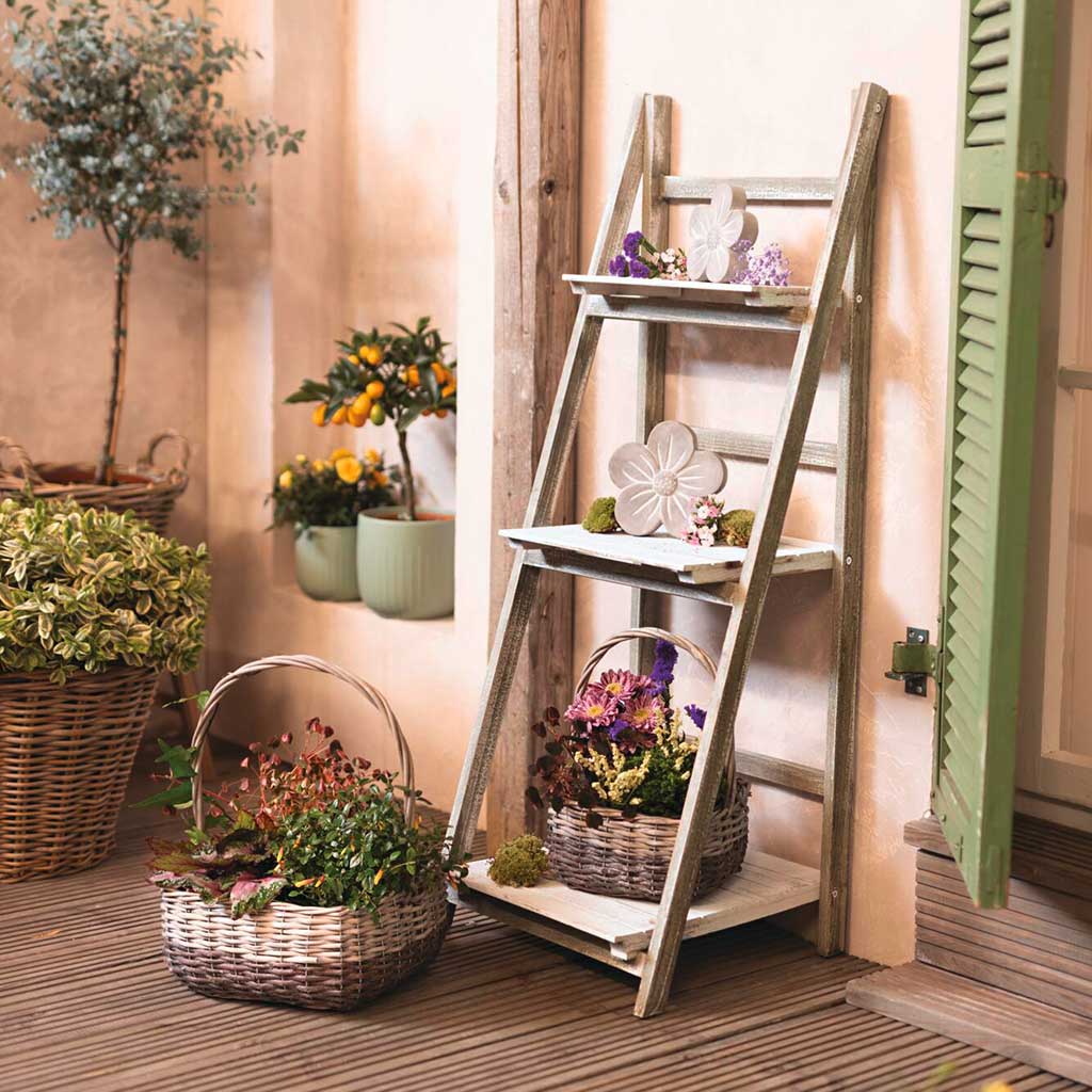 Gartendeko: graue Holzleiter mit Körben und Blumen als dekorative Pflanztreppe