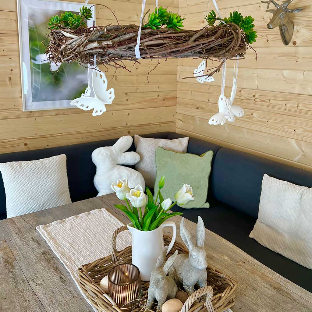 Osterdeko: Landhaus‑Tisch mit Hasenfiguren, Tulpen, Korbtablett und Naturmaterialien