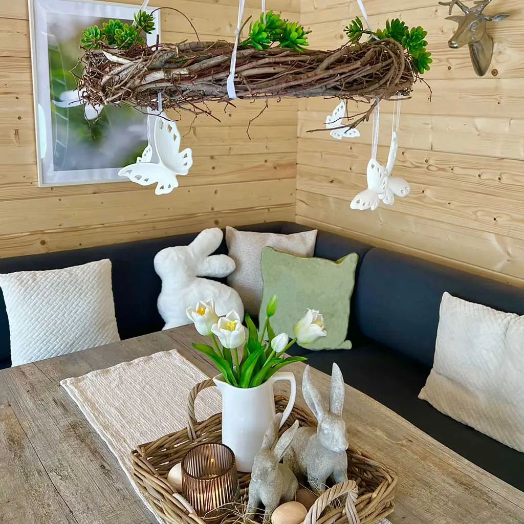 Osterdeko: Landhaus‑Tisch mit Hasenfiguren, Tulpen, Korbtablett und Naturmaterialien