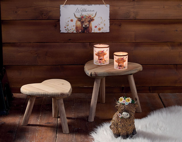 Hüttendeko: Holzhocker, Kerzen und Highland‑Rind Motiv als rustikale Dekoration im Alpenstil