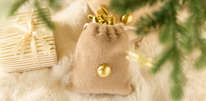 Weihnachtsdeko: beigefarbenes Samtsäckchen mit goldenen Christbaumkugeln auf weichem Fell