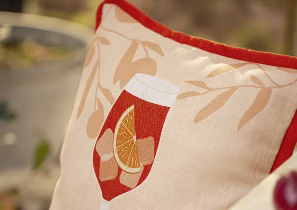 Geschenkgutschein mit Motiv einer Kissenhülle mit sommerlichem Getränk, Orangenscheibe und Eiswürfeln in warmen Rot- und Beigetönen