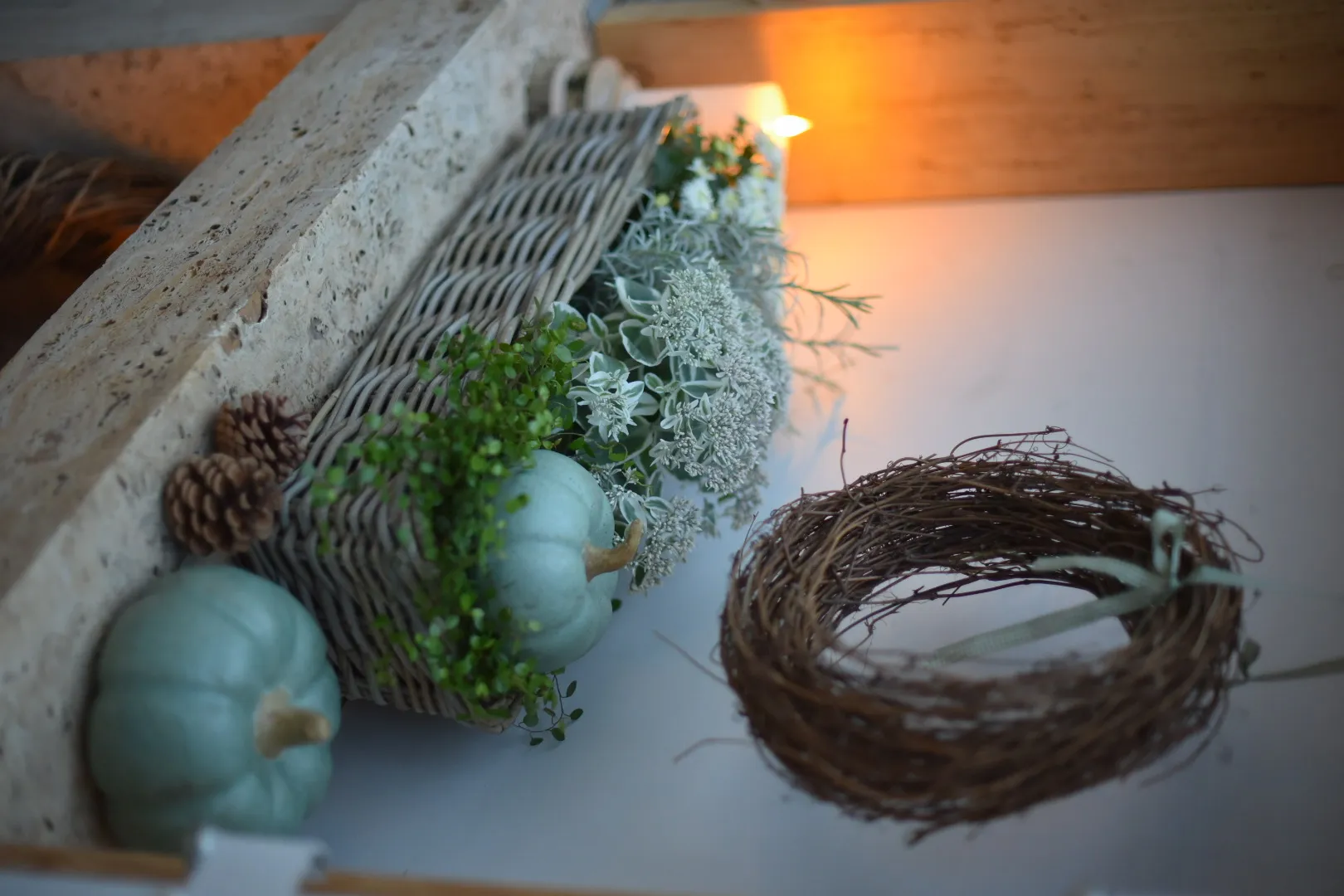 Herbstdeko: graue Zierkürbisse im Weidenkorb mit Naturkranz und weißen Blüten