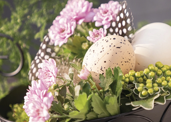 Osterdeko: gesprenkelte Dekoeier mit rosa Blumen und Federn als frühlingshafte Tischdekoration