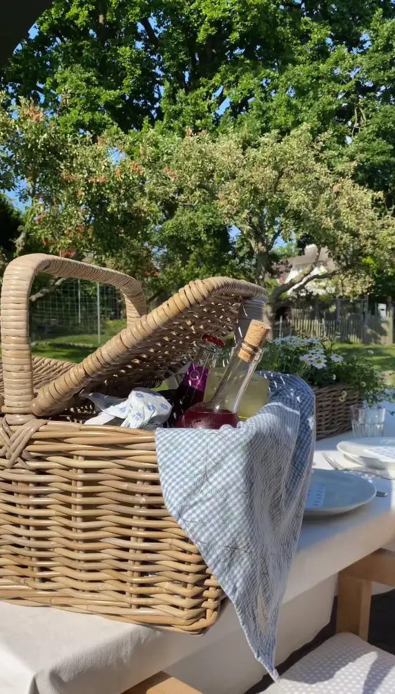 Picknickkorb: geflochtener Korb mit Getränken und Geschirr als sommerliche Gartenbegleitung