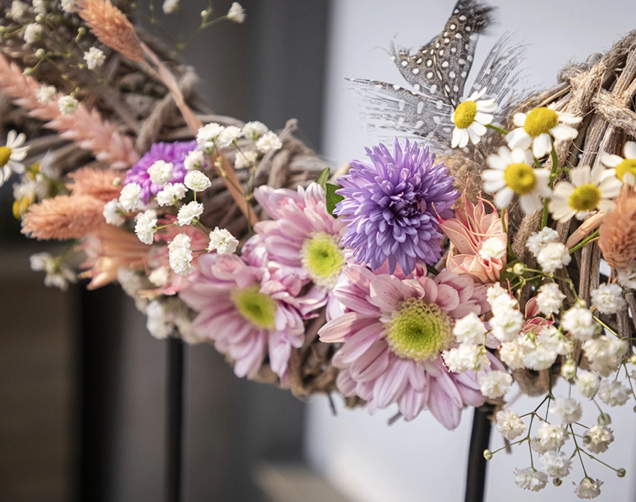 Dekokranz: geflochtener Kranz mit rosa und lila Blumen, weißen Blüten und Federn