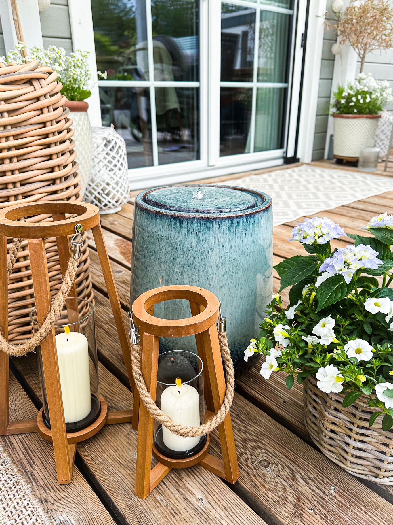 Gartendeko: Terrasse mit Holzlaternen, Kerzen, Pflanzkorb und blauen Hortensien im Außenbereich