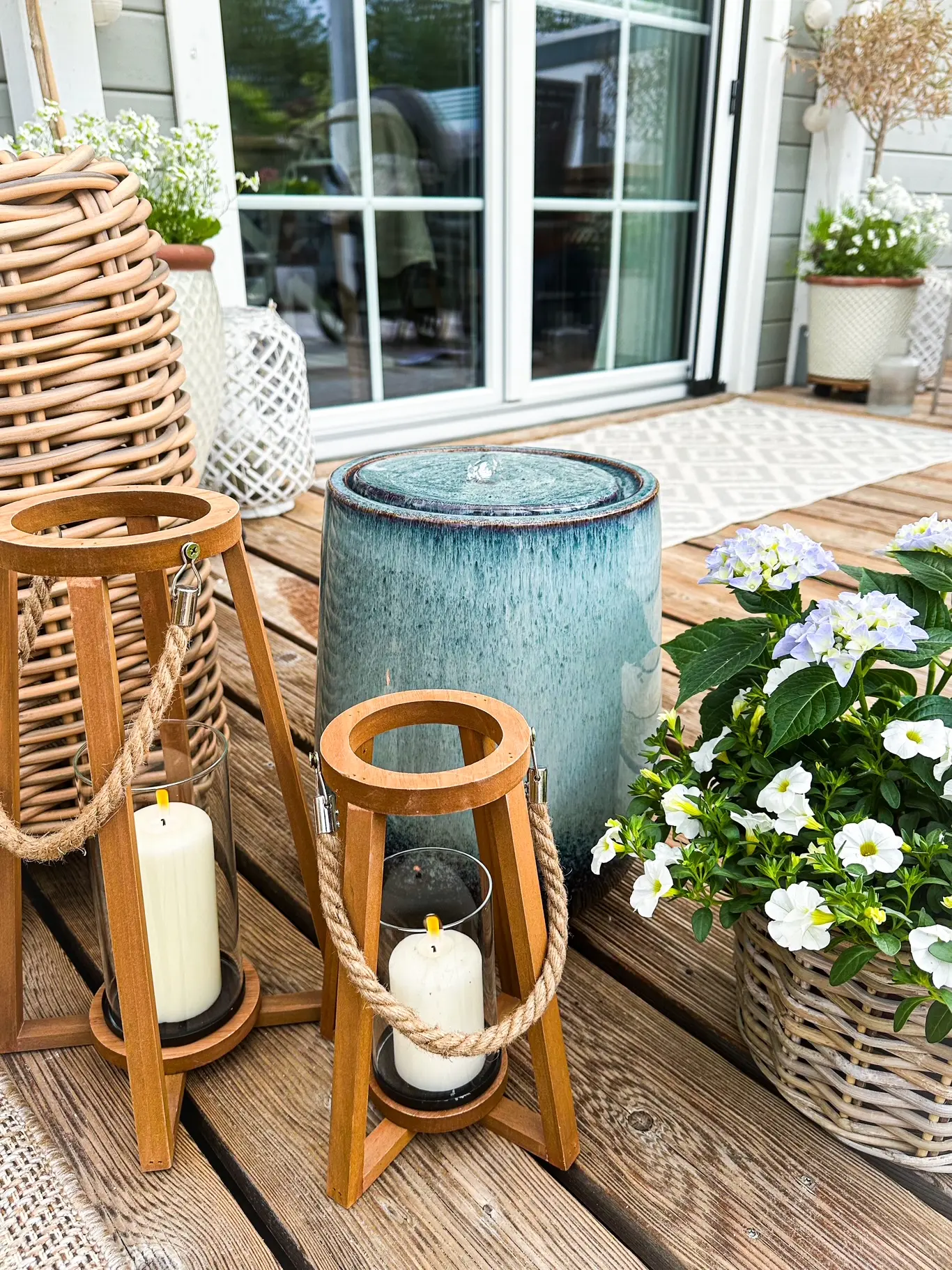 Gartendeko: Terrasse mit Holzlaternen, Kerzen, Pflanzkorb und blauen Hortensien im Außenbereich
