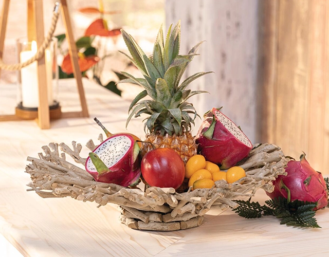 Tischdeko: Holzschale mit Ananas, Drachenfrucht und gelben Früchten als exotische Dekoration