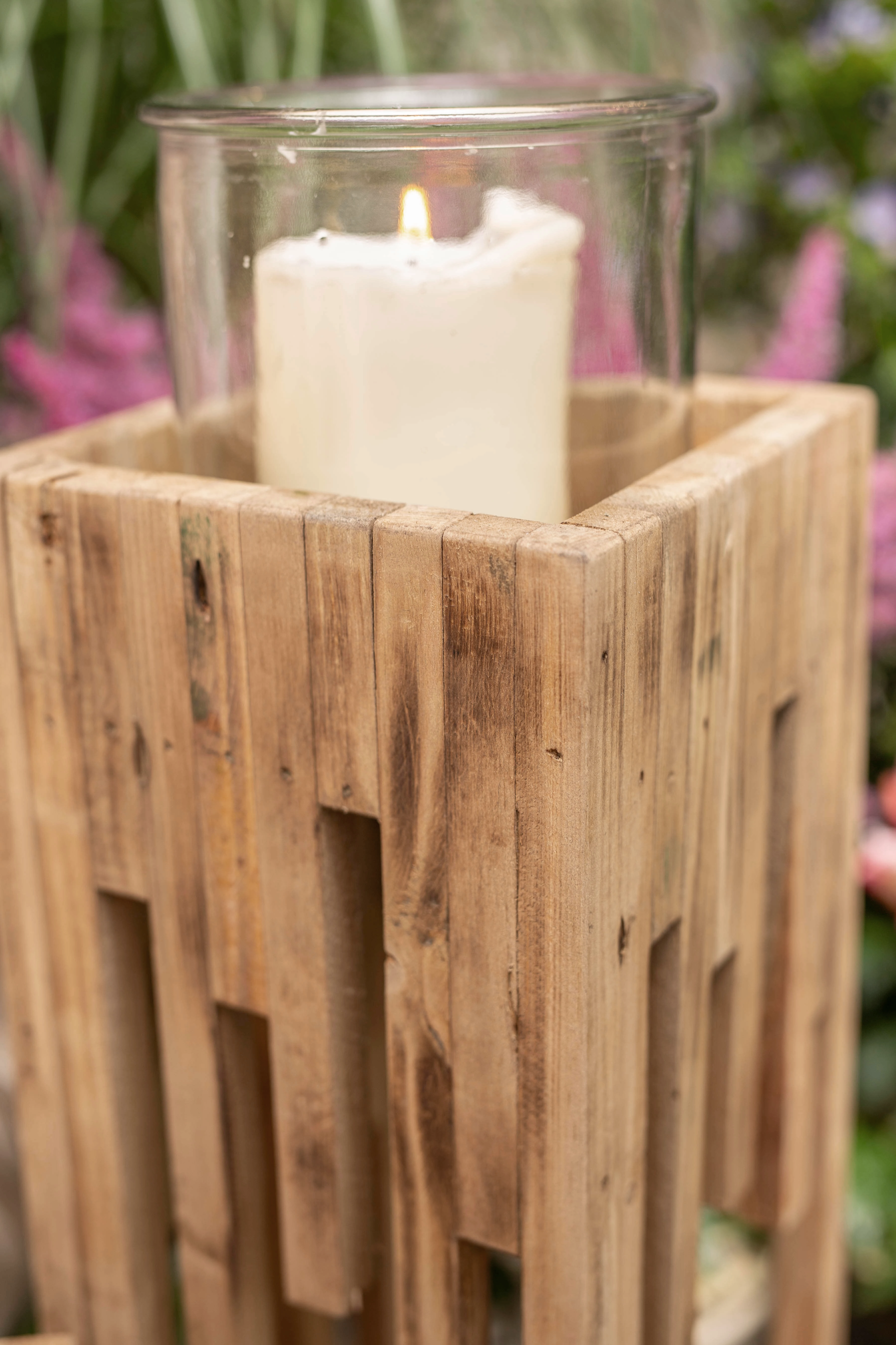 Rustikale Holzlaterne mit Glaseinsatz und brennender Kerze vor floralem Hintergrund in herbstlicher Dekoration
